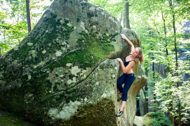 Junge Frau, die an Sommertag der im Freien der großen Flusssteine ​​klettert