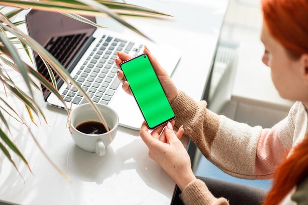 Junge Frau, die arbeitet und ihr Telefon überprüft. Konzentrieren Sie sich auf den Chromakey des Mobiltelefons, den grünen Bildschirm.