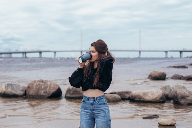 junge Frau, die auf das Meer schaut und Kaffee trinkt