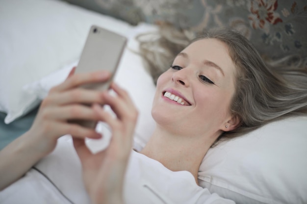 junge frau, die auf dem bett liegt, schreibt mit smartphone