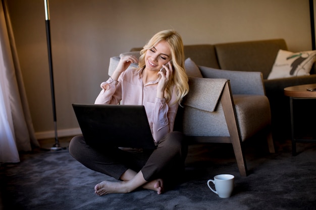 Junge Frau, die auf dem Boden im Raum mit Laptop sitzt