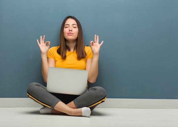 Junge Frau, die auf dem Boden mit einem Laptop durchführt Yoga sitzt