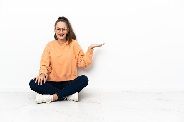 Junge Frau, die auf dem Boden sitzt und Kopienraum imaginär auf der Handfläche hält, um eine Anzeige einzufügen