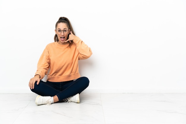 Foto junge frau, die auf dem boden sitzt und telefongeste macht. ruf mich zurück zeichen