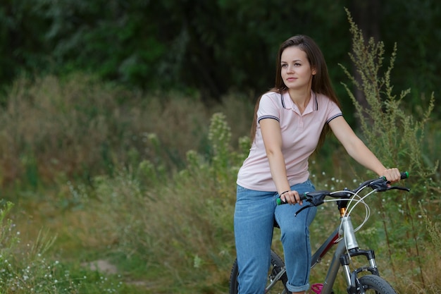 Junge Frau, die auf dem Fahrrad fährt und im Wald von der Kamera wegschaut, Kopienraum