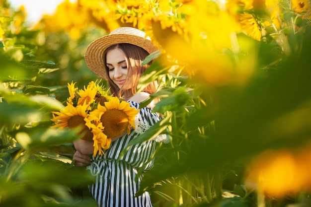 Junge Frau, die auf dem Feld in Richtung Sonne geht und eine Sonnenblume hält