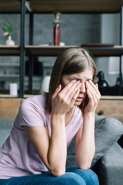 Junge Frau, die auf dem Sofa hat Augenschmerzen sitzt