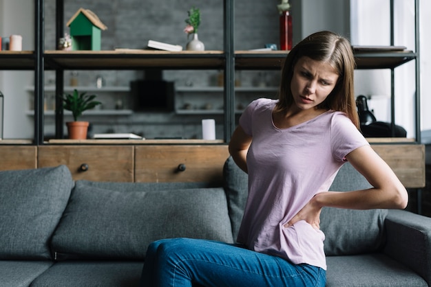 Foto junge frau, die auf dem sofa leiden unter rückenschmerzen sitzt