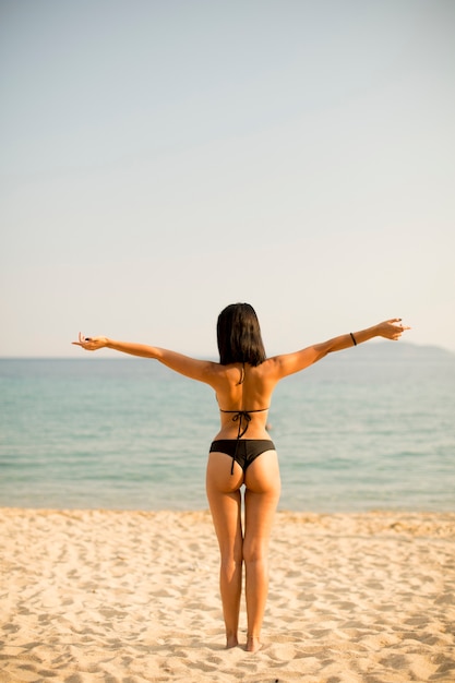 Junge Frau, die auf dem Strand in einem Bikini steht