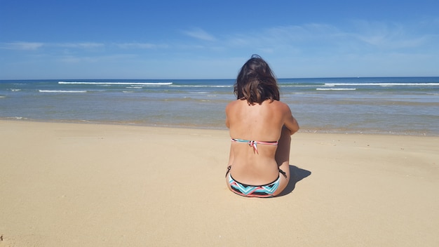 Junge Frau, die auf dem Strand sich entspannt am tropischen Erholungsort sitzt. Blick von hinten