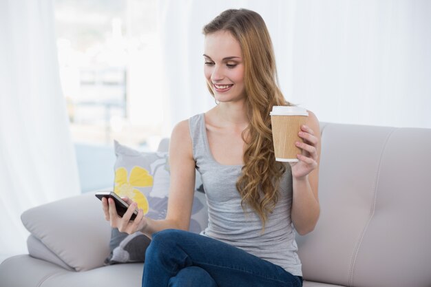 Junge Frau, die auf der Couch hält Wegwerfschale simst am Telefon sitzt