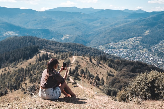 Junge Frau, die auf einem Felsen mit Rucksack sitzt und zum Horizont schaut