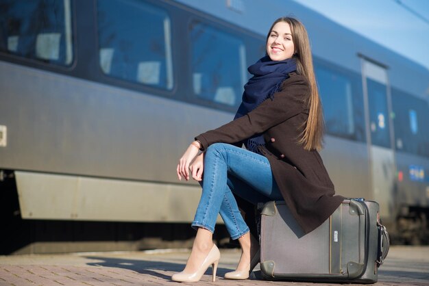 Junge Frau, die auf einem Koffer sitzt und am Bahnhof auf den Zug wartet