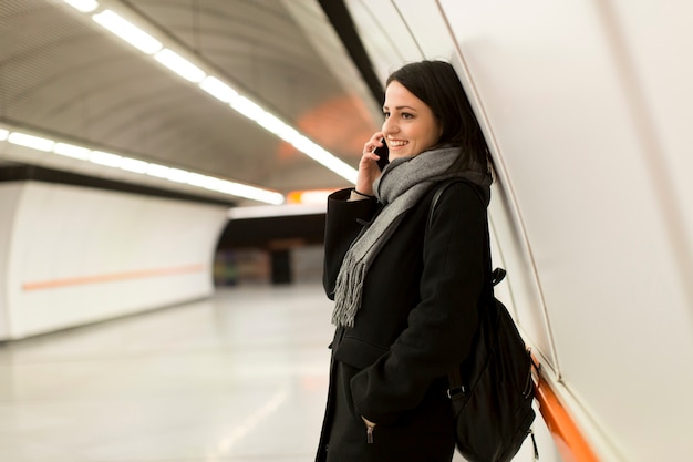 Junge Frau, die auf einer U-Bahnstation, Metro wartend steht und einen Handy verwendet