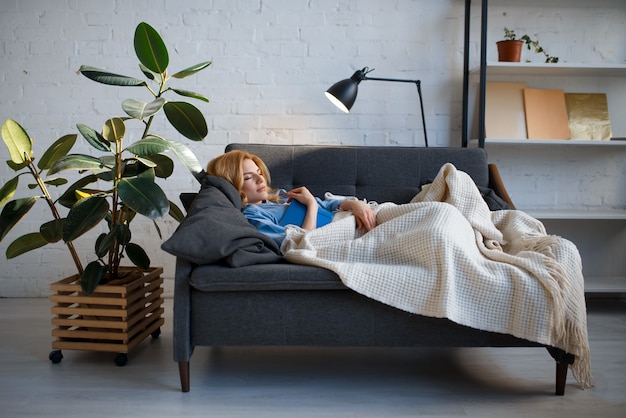 Junge Frau, die auf gemütlicher Couch liegt und ein Buch liest