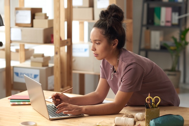 Junge Frau, die auf Laptop am Tisch in der Werkstatt tippt