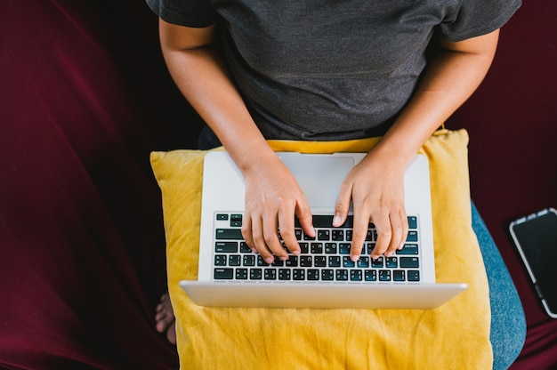 Junge Frau, die auf Laptop-Computer arbeitet, während auf dem Sofa am lebenden Haus sitzt