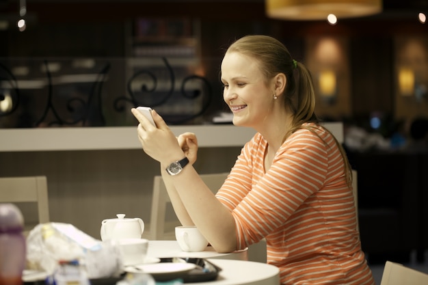 Junge Frau, die auf Smartphone im Café plaudert.