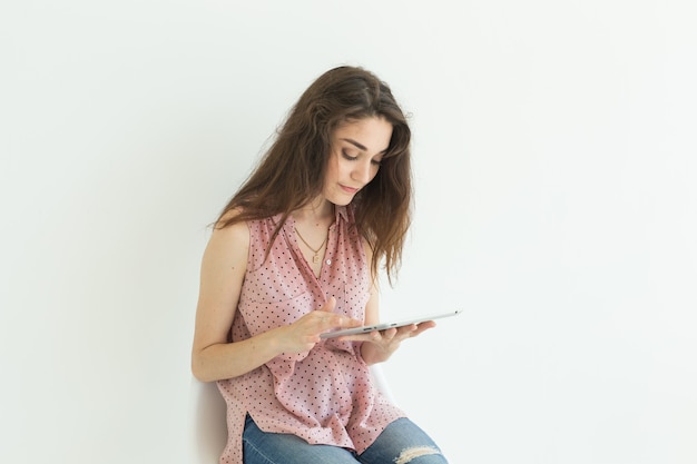 Junge Frau, die auf Stuhl sitzt, der mit einer Tablette auf weißer Wand arbeitet