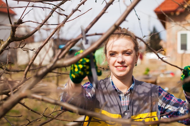 Junge Frau, die Bäume mit Baumscheren im Garten beschneidet Frau trägt Uniform und Handschuhe Gartenarbeitskonzept