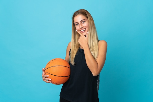 Junge Frau, die Basketball auf Weiß glücklich und lächelnd spielt