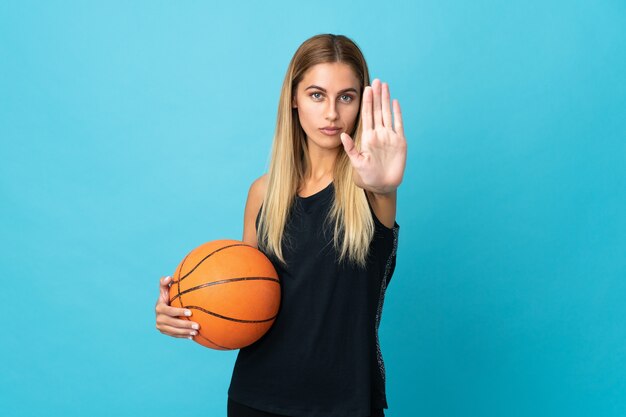 Junge Frau, die Basketball lokalisiert auf weißem Hintergrund spielt, der Stoppgeste macht