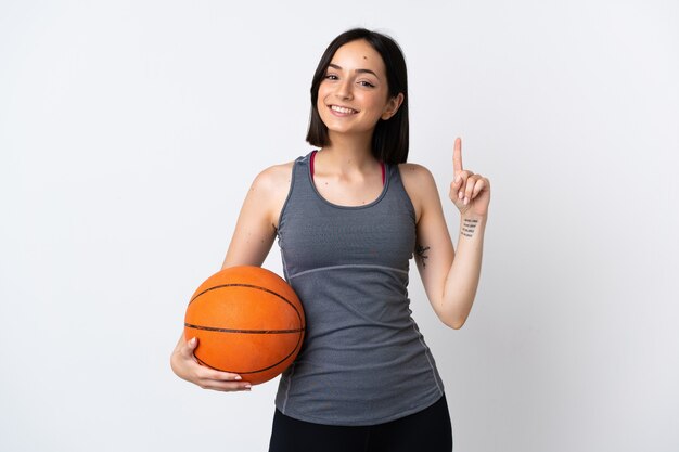 Junge Frau, die Basketball lokalisiert auf weißem Hintergrund spielt, zeigt eine große Idee auf