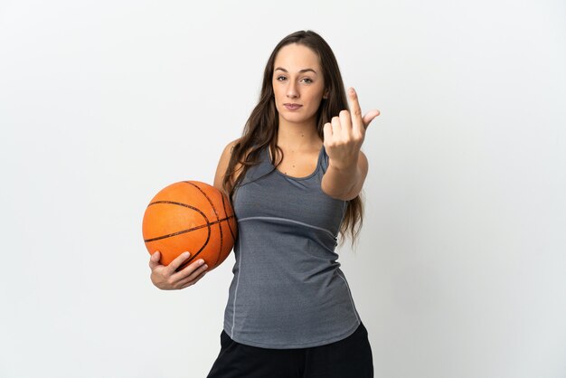 Junge Frau, die Basketball über isolierte weiße Wand spielt, die kommende Geste tut