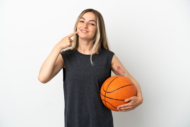 Junge Frau, die Basketball über isolierter weißer Wand spielt und eine Geste mit dem Daumen nach oben gibt