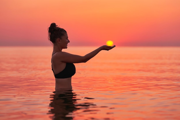 Junge Frau, die bei Sonnenaufgang im Meer schwimmt