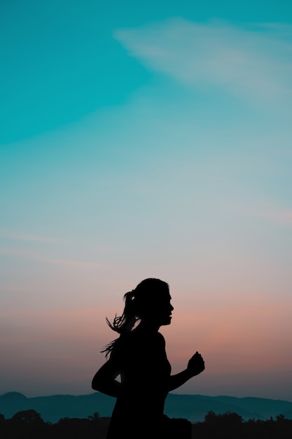 Junge Frau, die bei Sonnenaufgang mit natürlichem Hintergrund des Berges läuft.