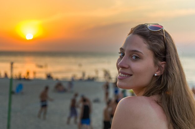 Junge Frau, die bei Sonnenuntergang am Strand in die Kamera blickt