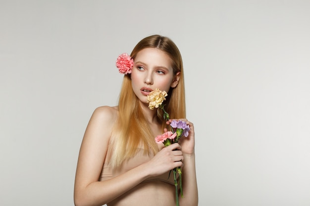 Junge Frau, die Blumen hält und in einem Studio aufwirft