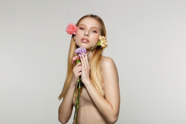 Junge Frau, die Blumen hält und in einem Studio aufwirft