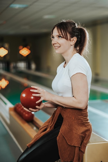 Junge Frau, die Bowlingkugel hält und sich darauf vorbereitet, den Bowlingclub einzuwerfen.