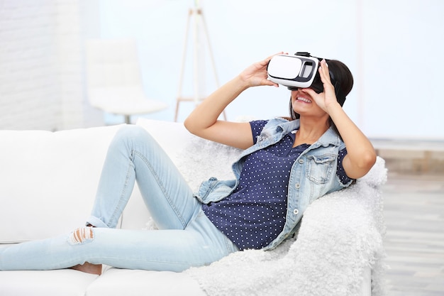 Junge Frau, die Brille der virtuellen Realität auf Sofa in einem Raum trägt