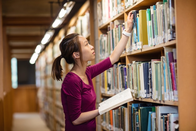 Junge Frau, die Buch in Bibliothek auswählt