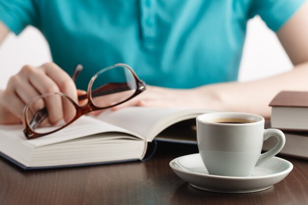 Junge Frau, die Buch liest und Brille in der Hand hält