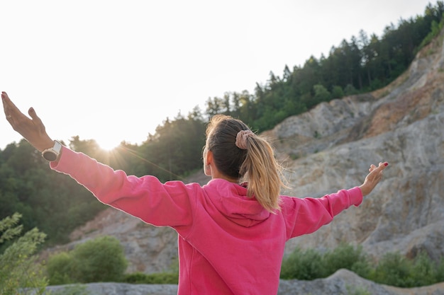 Junge Frau, die das Leben umarmt und mit weit ausgebreiteten Armen in der Natur steht