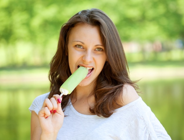 Junge Frau, die den sonnigen Tag der Eiscreme draußen isst