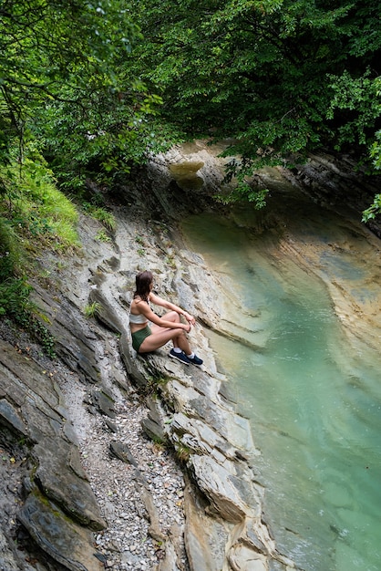 Junge Frau, die die Natur genießt, sitzt am Bergfluss