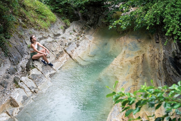 Junge Frau, die die Natur genießt, sitzt am Bergfluss