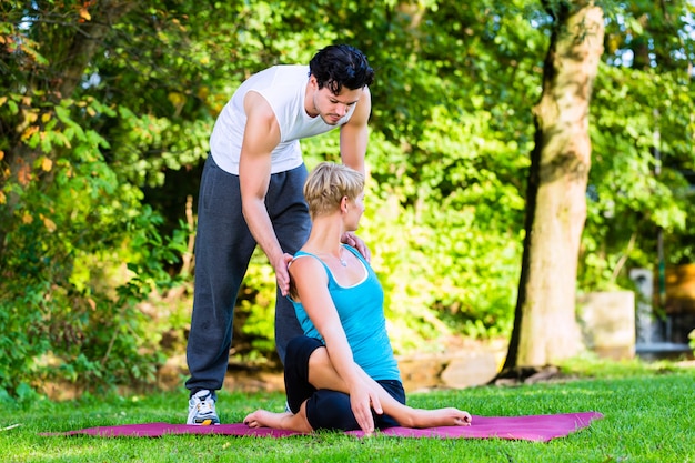 Junge Frau, die draußen Yoga mit Trainer tut