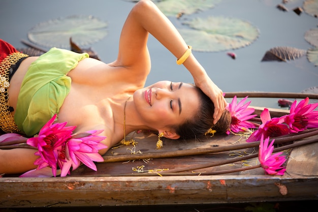 Junge Frau, die durch rosa Lotus On Boat In Lake liegt