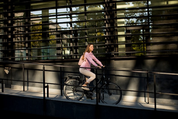 Junge Frau, die e Fahrrad in der städtischen Umgebung reitet