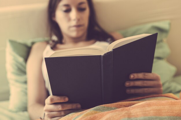 Junge Frau, die ein Buch auf dem Bett liest