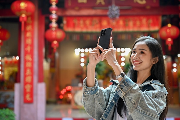 Junge Frau, die ein Foto mit Smartphone macht, während sie in einem traditionellen asiatischen Tempel unterwegs ist