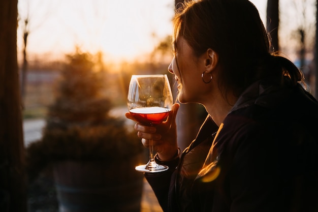 Foto junge frau, die ein glas rotwein im sonnenuntergangslicht draußen hält