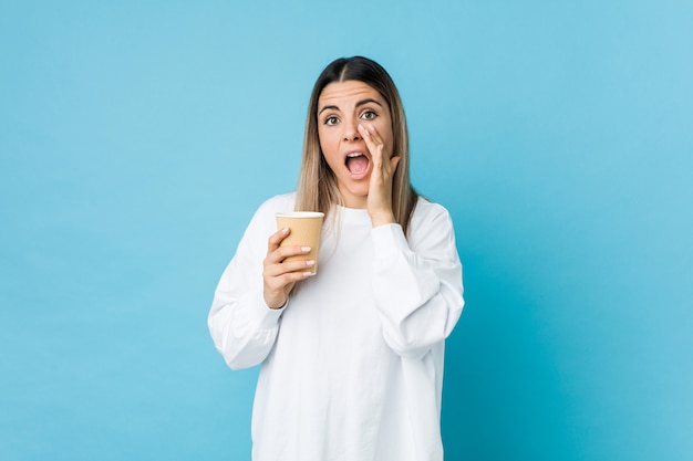 Junge Frau, die ein Mitnehmerkaffeeschreien aufgeregt zur Front hält