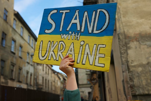 Junge Frau, die ein Plakat in den Farben der Nationalflagge und der Worte hält, steht mit der Ukraine im Freien in der Nähe